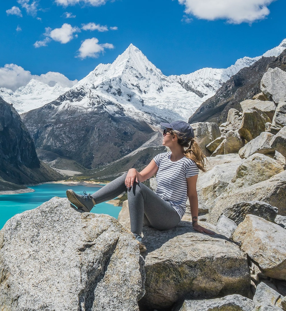 A traveler sitting on a rock overlooking a turquoise Andean lake
